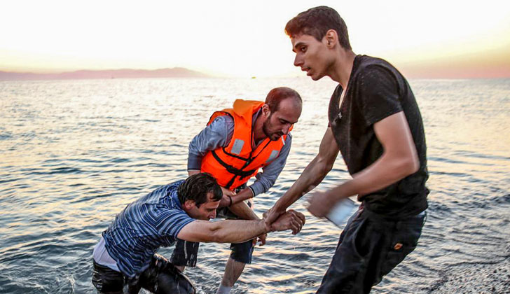 Un refugiado sirio exhausto es ayudado por voluntarios de una ONG, al llegar después de haber cruzado el Mar Egeo. Foto: Freedom House. 