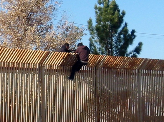 Dos hombres escalan el muro fronterizo entre México y Estados Unidos. Foto: Wikimedia Commons 