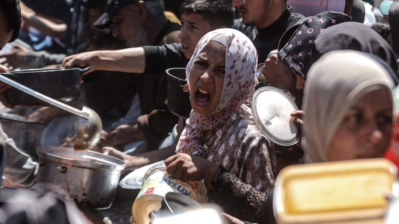Una mujer gazatí, rodeada de cientos de otras personas, grita desesperada por un plato de comida. Foto cortesía de la agencia de noticias palestina WAFA