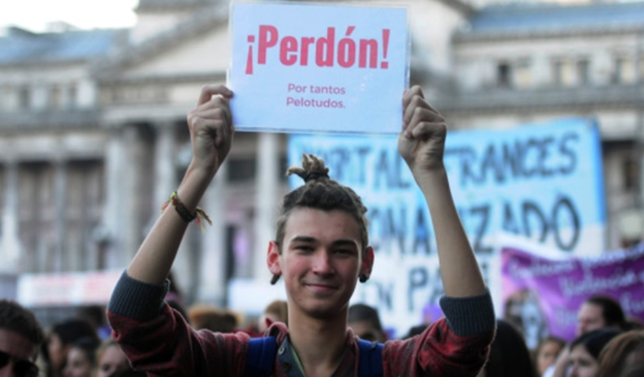 Un joven activista en una marcha en el Congreso argentino sostiene un cartel que dice "Perdón, por tantos pelotudos".