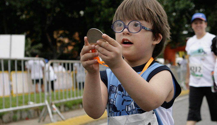 Un niño con síndrome de down corre en una carrera, a la vez que sostiene una medalla ganada. Foto con fines ilustrativos: Wikimedia Commons. 