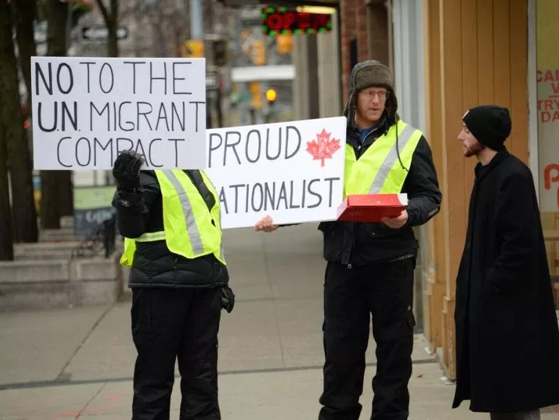 Manifestantes sostienen carteles que dicen "No al pacto migratorio de la ONU" y orgulloso nacionalista". Foto cortesía del Windsor Star de Canadá