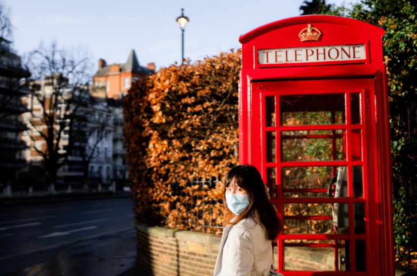 Una mujer camina frente a una clásica casetilla telefónica inglesa. Foto: UNsplash / Johen Redman