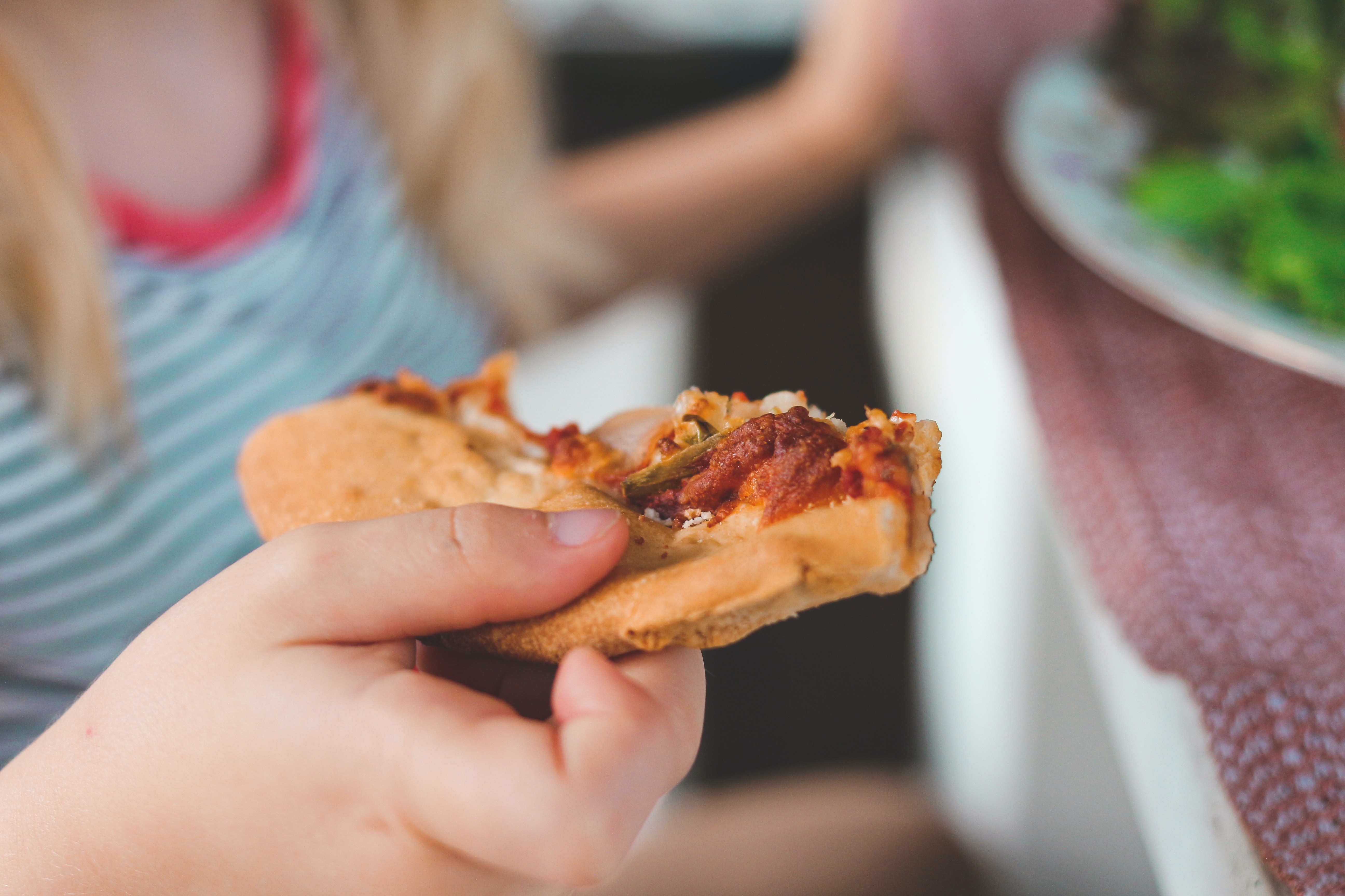 Una niña come una porción de pizza, comida que en muchos países se vende bajo los estándares de ultraprocesamiento y son altos en ingredientes poco saludables. Foto: UNsplash / @sigmund