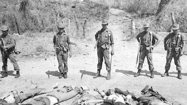 Militares posan para la cámara frente a decenas de cadáveres de civiles inocentes asesinados en la masacre de El Mozote. Foto desclasificada por el gobierno de El Salvador