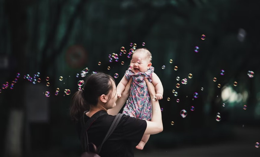 Una mujer sostiene a su bebé en un parque de Shanghái, China. Foto: UNsplash / Rui Xu