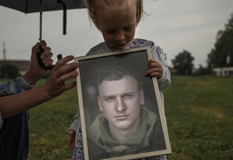 Yuliia sostiene un retrato de su padre junto a su tumba. El mayor Andrii Verkhohliad fue asesinado en la región de Donetsk a manos de fuerzas rusas. Foto: Twitter / DefenceU