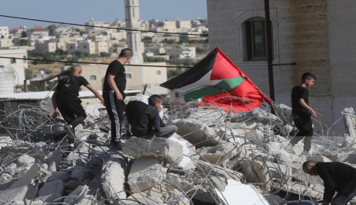 Jóvenes ondean una bandera de Palestina sobre los restos de un edificio bombardeado por Israel. Foto cortesía de la agencia de noticias palestina Wafa